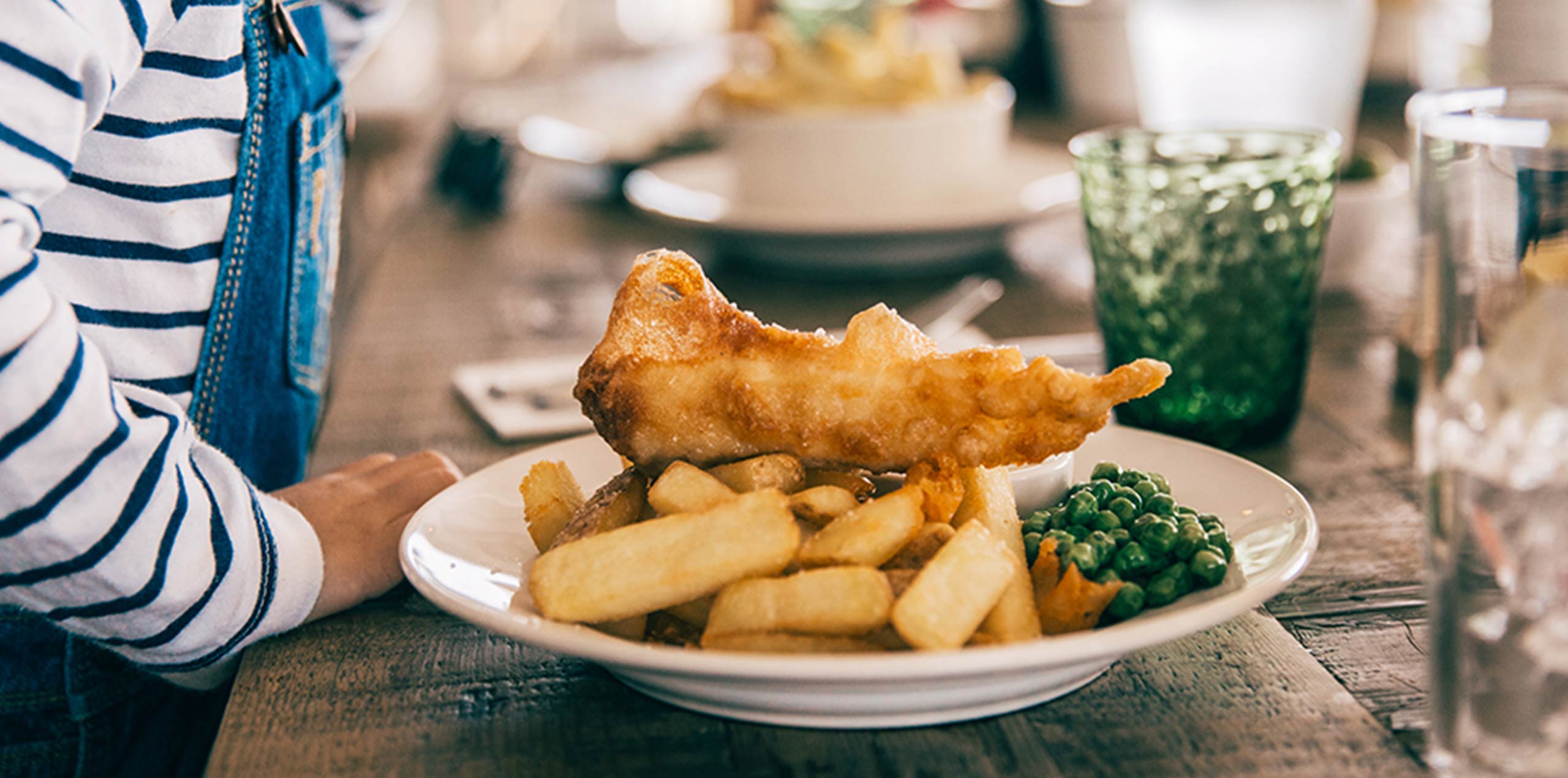 An image of fish, chips and peas on a white plate. 